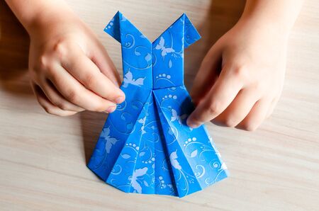 Kid's hands holding origami made blue dress from butterfly printed paper.の写真素材