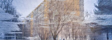 Blurry reflection of residential building and trees in a puddle on wet city street during rainy day. Autumn banner, abstract background. Mood meditative concept.の写真素材