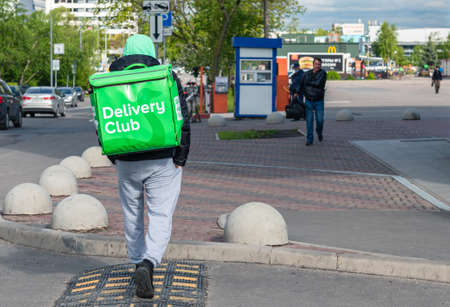 Moscow, Russia-May, 2020: Delivery club courier carrying food delivery green box with company logo walking down the street to McDonalds restaurant. Fast food delivery company deliveryman.のeditorial素材