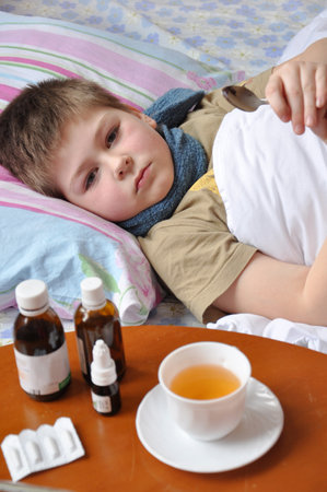 Sick boy lying in bed. Drugs on the tableの写真素材