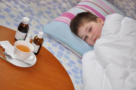 Sick boy lying in bed. Drugs on the tableの写真素材
