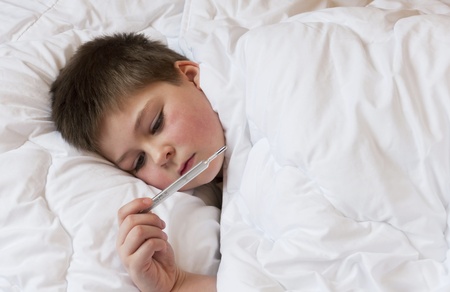 Sick boy looks at the thermometer. Bed restの写真素材