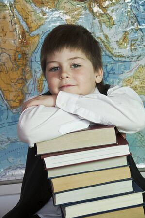 Schoolboy with a stack of books on a background map of the worldの写真素材