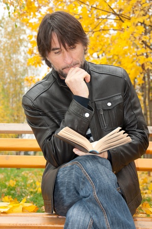 Middle-aged man with a book in autumn parkの写真素材