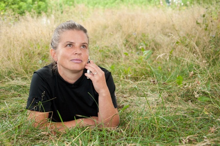 Middle-aged woman with the phone lying on a meadowの写真素材
