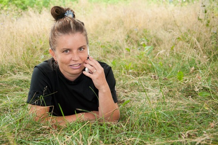 Middle-aged woman with the phone lying on a meadowの写真素材