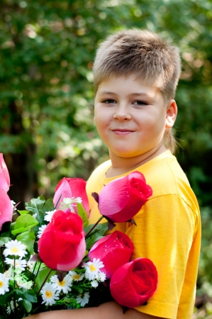 A boy with a bouquet of artificial flowers in summer parkの写真素材