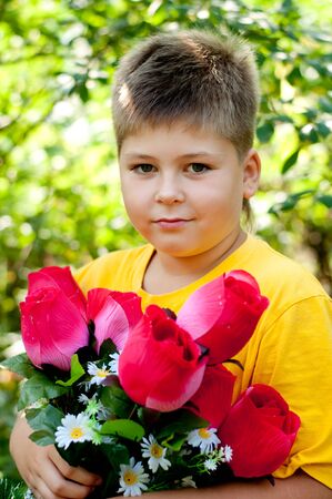 A boy with a bouquet of artificial flowers in summer parkの写真素材