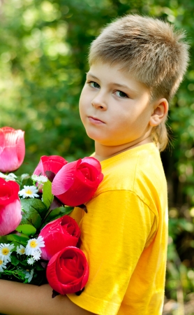 A boy with a bouquet of artificial flowers in summer parkの写真素材