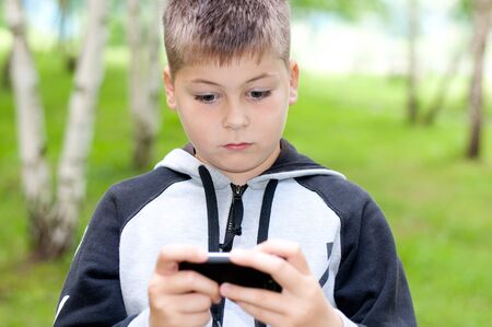 A boy plays on a mobile phone in a parkの写真素材