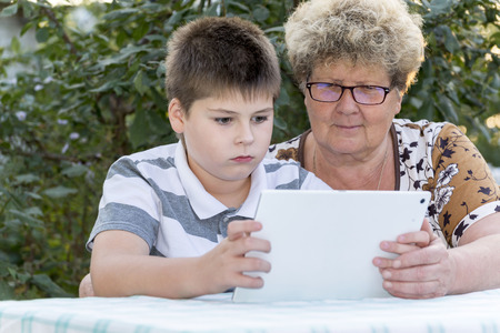 Granny with a grandson watching tablet in natureの写真素材