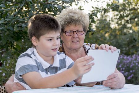 Granny with a grandson watching tablet in natureの写真素材