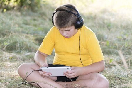Boy in headphones looking at tablet computer on the natureの写真素材