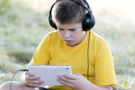 Boy in headphones looking at tablet computer on the natureの写真素材