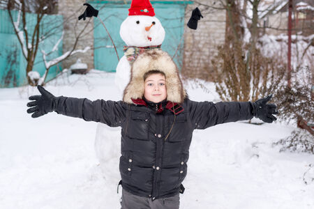 The boy in a fur hat near snowmanの写真素材