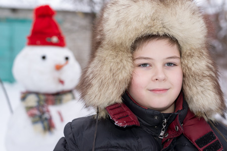 The boy in a fur hat near snowmanの写真素材
