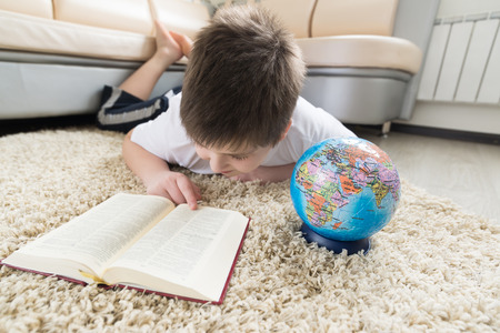 Boy studying the globe and reading a bookの写真素材