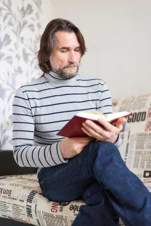 Bearded man reading a book in the living roomの写真素材