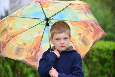 Outdoor portrait of adorable little blond boy with umbrella under the rainの写真素材