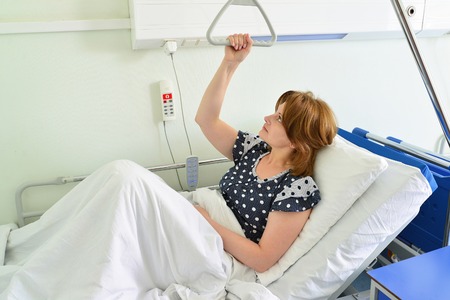 Female patient holding on to a device for lifting in hospital roomの写真素材