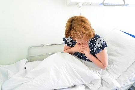 Female patient With heartfelt pain lying on a bed in hospital wardの写真素材
