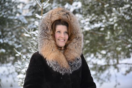 Positive middle-aged woman in a fur coat in the winter park