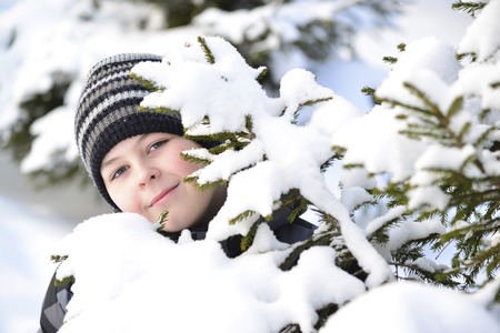 Teen boy looks out from behind trees in the winter forest