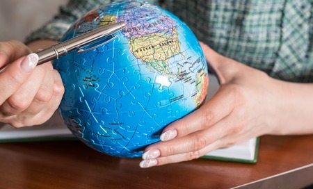 Female hand with a pen and a globe of the puzzleの写真素材