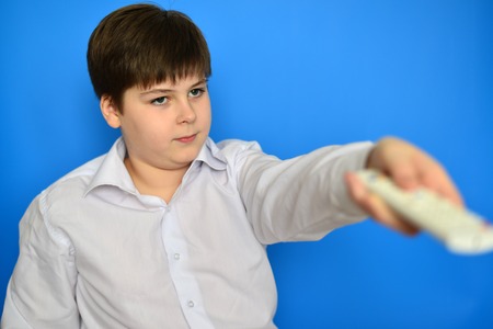 Boy teenager with the TV remote control on a blue backgroundの写真素材