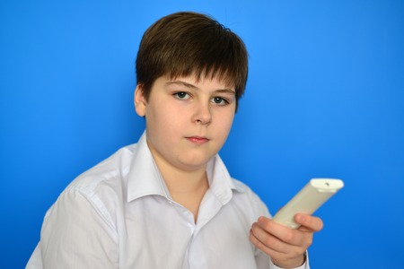 Boy teenager with the TV remote control on a blue backgroundの写真素材