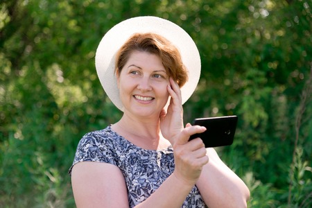 A woman in a hat with cell phone outsideの写真素材