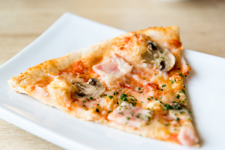 piece of pizza with mushrooms and ham on a plateの写真素材