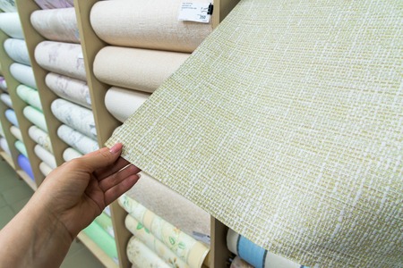 female hand holding a beige wallpaper in storeの写真素材