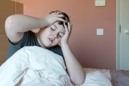 boy with headache sitting in bedの写真素材
