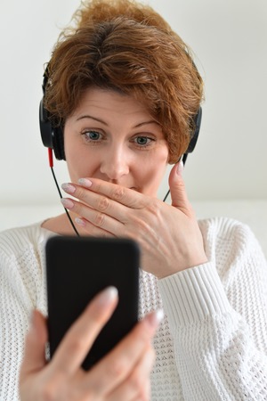Woman in headphones with surprise looks at smartphone