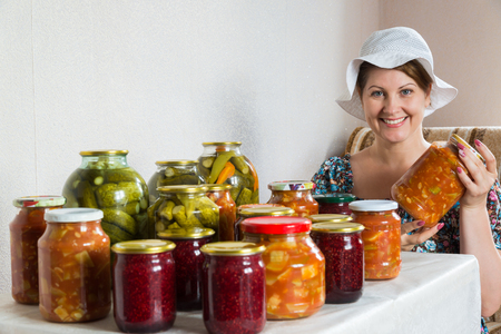 woman sits at table with homemade canned vegetables and jamの写真素材