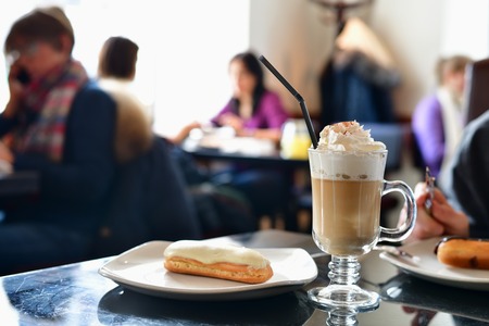 coffee with whipped cream and eclair on the table in a cafe