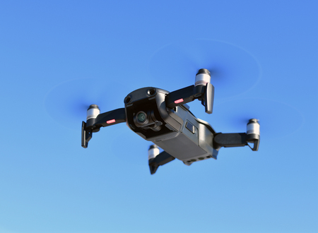 Black unmanned aerial vehicle with a camera against the blue sky.
