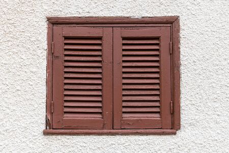 Closed window with a brown shutters on a light wallの写真素材