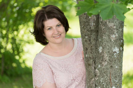 brunette woman near tree in summer parkの写真素材