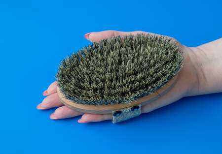 Massage brush with natural boar bristles in a woman hand on a blue backgroundの写真素材