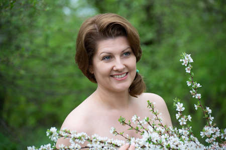 Portrait of middle-aged woman with bare shoulders near a cherry blossomの写真素材