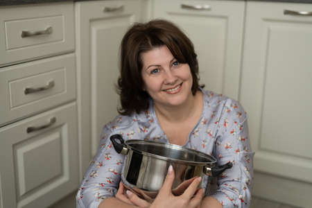 Portrait of a smiling woman holding an empty pan on background of the kitchenの写真素材