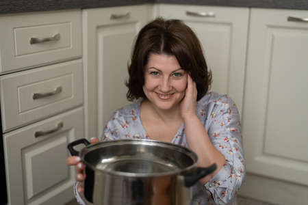 Portrait of a smiling woman holding an empty pan on background of the kitchenの写真素材