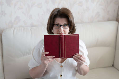 Woman with glasses with a book sitting on the sofaの写真素材