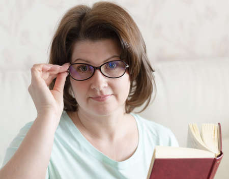 Woman with glasses with a book sitting on the sofaの写真素材