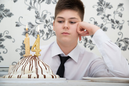 teen boy at table with cake for his fourteenth birthdayの写真素材