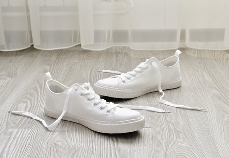 White sneakers with untied laces are on the floorの写真素材