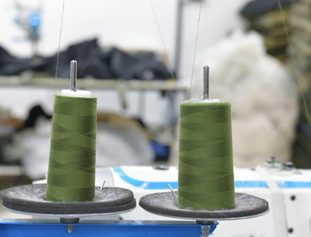 Two large spools of green thread on the background of clothing industry