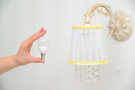 LED light bulb in a female hand against the background of a sconceの写真素材